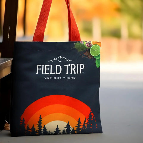The Field Trip Gift Bag | Jerky & Meat Sticks by Field Trip features orange handles and a nature-themed design with trees, a sunset, lime slices, and autumn colors—perfect for carrying your favorite treats or as a thoughtful gift.
