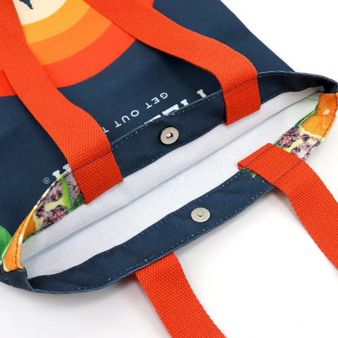 Close-up of the Field Trip Gift Bag | Jerky & Meat Sticks by Field Trip, featuring bright orange handles, a magnetic snap closure, dark blue fabric with colorful prints, and a white lining—ideal for carrying jerky or a gift set.