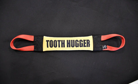 The Bulletproof Pet Products Inc Tooth Hugger Fire Hose Training Tug is a USA-made tug with red loops at each end and a yellow TOOTH HUGGER center, shown on a plain black background.