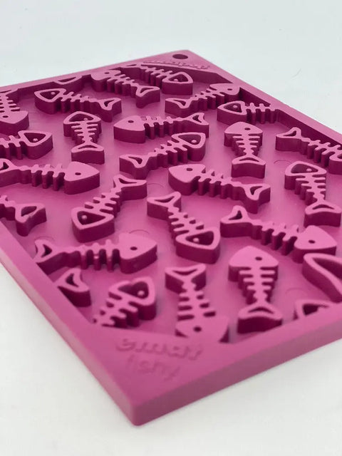 The SodaPup Fishy Design EMat Enrichment Lick Mat - Small, a pink silicone mat with multiple fish-shaped cavities, is perfect for calming dogs and cats or making treats and ice cubes, and is shown on a white surface.