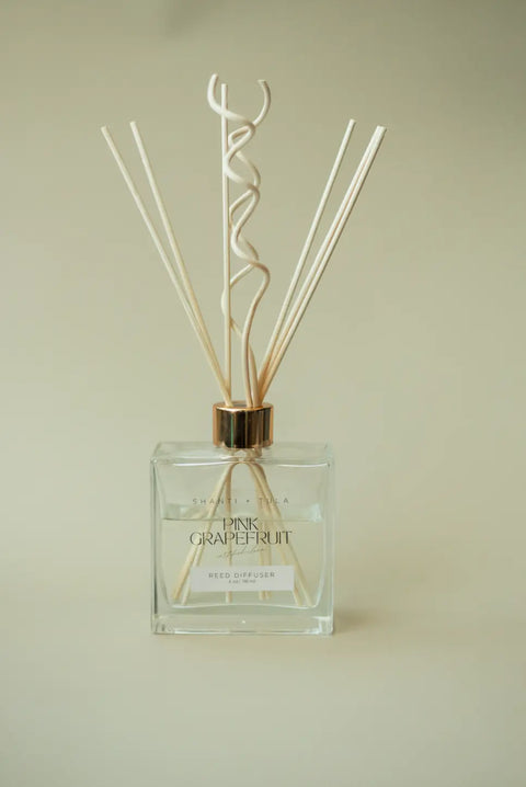 The Shanti + Tula Flame-Free Reed Diffuser features natural-colored reeds and spiral sticks in clear glass with a gold cap, offering long-lasting Pink Grapefruit aromatherapy—perfect for adding vibrant fragrance to your home or office. Made in the USA.