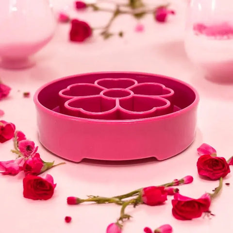 A pink Flower Design EBowl Enrichment Slow Feeder Bowl for Dogs by SodaPup is displayed on a light pink surface, surrounded by scattered red and pink flowers for an enrichment-inspired look.