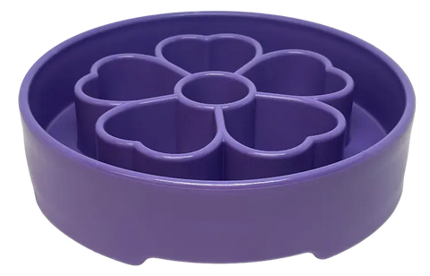 The SodaPup Flower Design EBowl Enrichment Slow Feeder Bowl for Dogs is a round, purple plastic bowl with six heart-shaped compartments arranged in a flower pattern around a central circle.