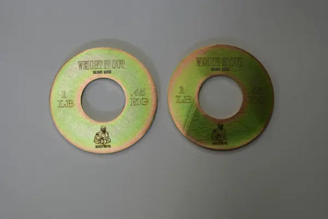 Two Fractional Solid Steel Mini Olympic Weight Plates by Weight It Out rest on a gray surface. Each is marked 1 LB, 0.45 KG, and features a muscular figure logo—perfect for adding precise weight to your Olympic bar.