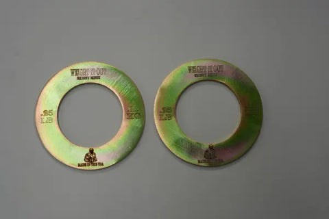 Two Fractional Solid Steel Mini Olympic Weight Plates by Weight It Out, each 2.5 LB and MADE IN THE USA, sit side by side on a gray surface. They have large central holes to fit an Olympic bar for gradual weight increase.