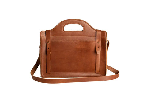 The Urban Southern Franklin Satchel is a brown leather bag featuring a handle cutout, front pocket, two vertical straps, and an adjustable shoulder strap, shown against a white background.