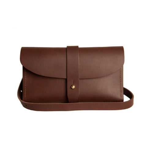 The Urban Southern Crossbody Wallet is a brown leather bag with a minimalist design, featuring a flap closure with strap and metal button, shown on a plain white background.