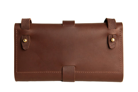 The Urban Southern Crossbody Wallet is a brown leather pouch with stitched edges and two leather straps with brass studs, offering minimalist design and maximum organization, shown against a white background.