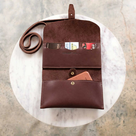 The Urban Southern Crossbody Wallet, shown open on a round white table, reveals its suede interior with cards and a brown phone wallet inside. This minimalist accessory features a long strap for easy organization and carrying.