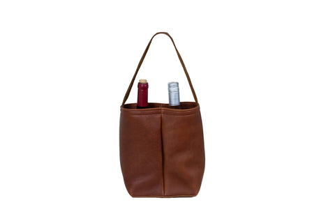 The Urban Southern Urban Dual Wine Tote is a brown leather carrier with two compartments, each holding a wine bottle—one with a red cap and one with a silver cap—displayed against a white background.