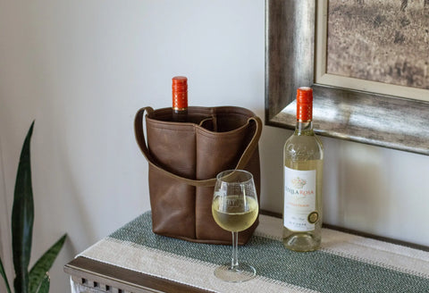 An Urban Southern Urban Dual Wine Tote holding a bottle stands beside a Stella Rosa wine bottle and filled glass on a table runner near a plant, with a framed picture displayed on the wall.