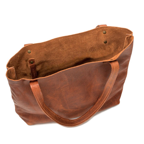 The Fore Street Tote Bag by Rogue Industries is a brown full-grain leather tote with two handles, an open top, spacious unlined interior, and small metal button accents near the handles.