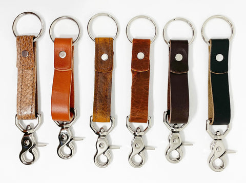 Six Rogue Industries Leather Key Chains, made of durable top-grain cowhide in brown and black hues, each featuring a metal keyring and silver swivel clasp, stand upright in a row on a white background.