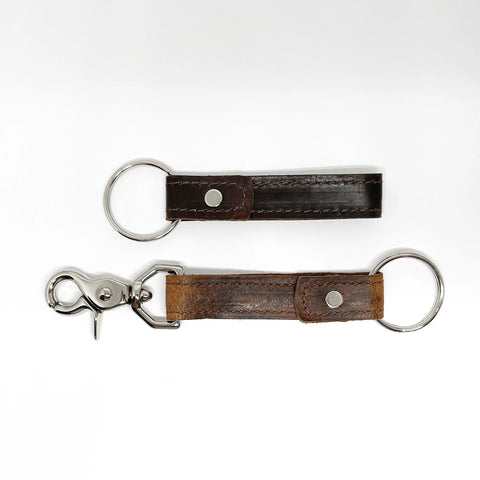 Two Rogue Industries Leather Key Chains are shown on a white background: one dark brown and plain with a metal key ring, the other light brown with a metal clasp. Both are crafted from durable top-grain cowhide.