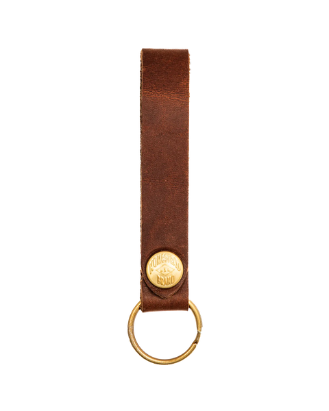 The Standard Key Fob No. 1603 by Homestead Brand features USA-tanned brown leather, an oval gold metal plate engraved with Homestead Brand, a brass ring, and solid brass hardware.