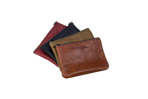 Four small Urban Southern Zipper Pouch pouches in brown, tan, black, and red are stacked on a white background. The front pouch features a sleek gold zipper and Urban Southern branding.
