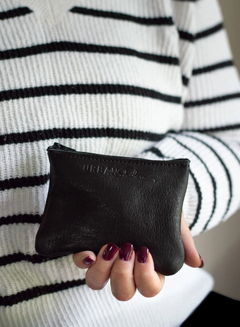A person with dark burgundy nails, wearing a white and black striped sweater, holds the Urban Southern Zipper Pouch—a small garment leather pouch featuring a gold zipper closure.