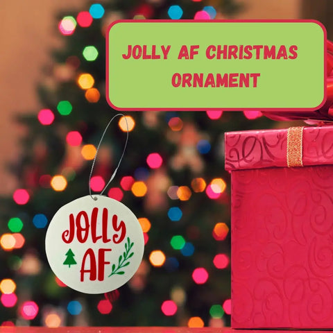 A round Chatelet Manufacturing ornament reading Jolly AF hangs by a pink gift box, making this Funny Gag Gift Christmas Ornament the perfect Dirty Santa gift. Made in USA. Text above reads: Jolly AF Christmas Ornament.