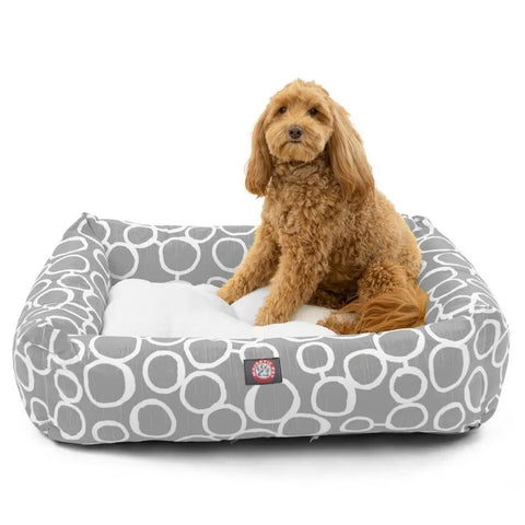 A fluffy, caramel-colored dog sits on the Majestic Pet Fusion Luxe Bagel Bed—a gray, circular-patterned, machine-washable pet bed with a soft white cushion.