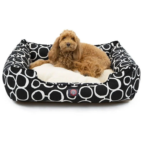 A fluffy, light brown dog relaxes on a cream cushion in the Majestic Pet Fusion Contemporary Lounge Bed, featuring durable upholstery with large white circles. The dog is facing the camera and looks at ease.