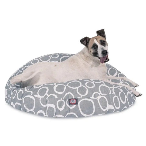A relaxed dog lounges on the Majestic Pet Fusion Round Dog Bed. This gray bed features white circular patterns and a washable, removable cover to keep it fresh, as the light-colored dog with dark markings looks at the camera.