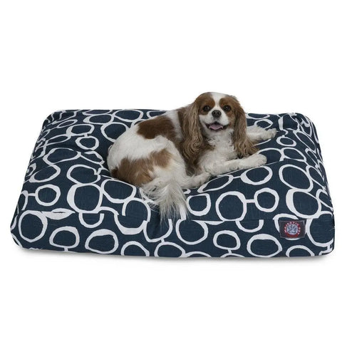 A brown and white dog lounges on the Majestic Pet Fusion Memory Foam Dog Bed, a blue-and-white patterned rectangular bed, gazing at the camera with its mouth slightly open.