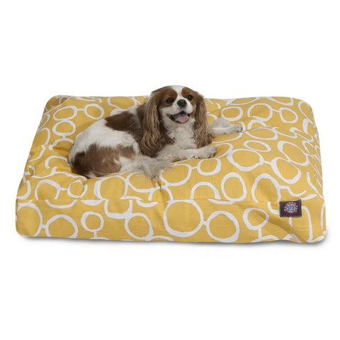 A brown and white dog lies on the Majestic Pet Fusion Memory Foam Dog Bed—a rectangular yellow bed with a white circular pattern and washable cover. Shredded memory foam keeps your pup relaxed, tongue out and tail curled beside it.