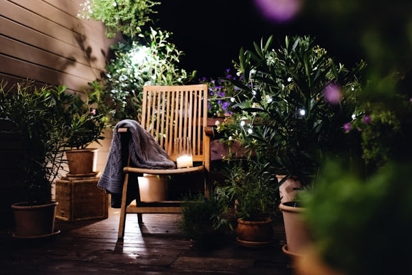 Wooden chair with a blanket on a patio surrounded by potted plants at night.