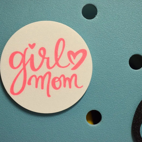 The FRESHe BOGLETS Girl Mom Charm by Chatelet Manufacturing is a pink and white decorative magnet accessory for Bogg Bags, featuring “girl mom” in pink cursive with a heart, perfect for personalizing your bag.