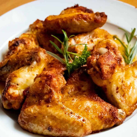 Golden-brown air fryer chicken wings seasoned with Gustus Vitae’s Global Chicken Air Fryer Seasoning Set—Artisanal Spice Blends Six Pack—garnished with fresh rosemary and parsley, served on a white dish.