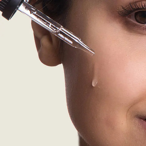 A close-up of a woman’s face with a dropper applying Open Formulas Glycolic Acid Peel to her cheek, highlighting smooth skin as the formula exfoliates dead skin cells.