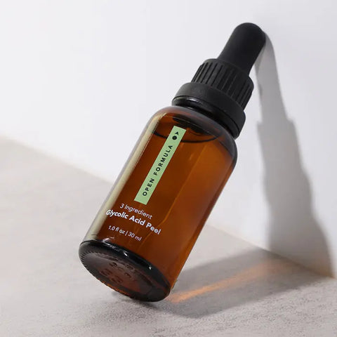 A brown glass dropper bottle labeled Open Formula Glycolic Acid Peel, 1 oz/30 ml, sits upright on a light surface with a shadow—this exfoliating solution removes dead skin cells for a brighter look.