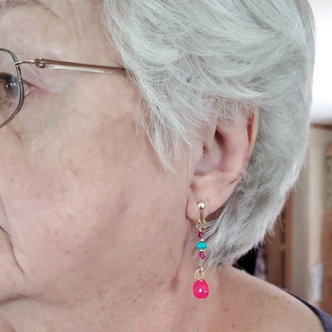 Close-up of an older woman with short white hair and glasses wearing Alexa Martha Designs Gold Filled Wire Wrapped Pink and Turquoise Gemstone Earring. Only the left side of her face and ear is visible.