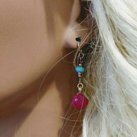 A woman with long blonde hair wears Alexa Martha Designs’ Gold Filled Wire Wrapped Pink and Turquoise Gemstone Earrings, featuring a turquoise bead and a bright pink teardrop charm.