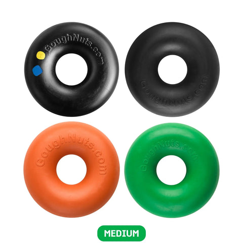 Four Goughnuts Medium Rings dog toys (for dogs 30-70 lbs) in black, orange, green, and black with colored dots are arranged in a square on white. Each is labeled GoughNuts.com. A green “MEDIUM” label appears below. Backed by the Goughnuts Guarantee.