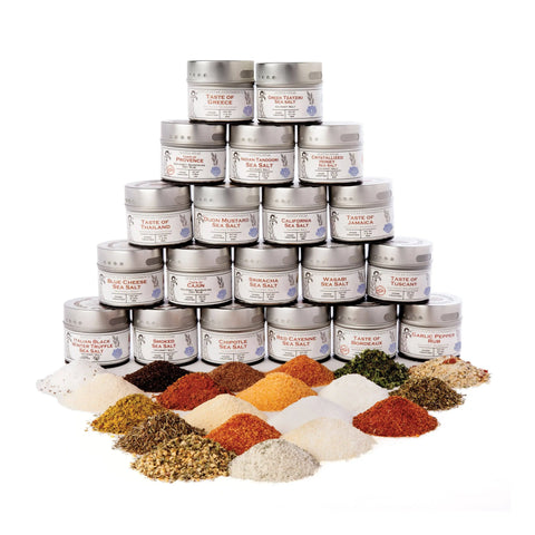 A pyramid of Gustus Vitae’s Ultimate Artisanal Seasoning and Gourmet Sea Salt Collection—20 tins—is stacked behind vibrant piles of salts and seasonings, all artfully arranged on a white background.