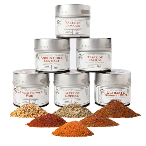 Six tins from the Gustus Vitae Ultimate Gourmet BBQ Collection are stacked, each with a colorful spice pile in front, all set against a white background.