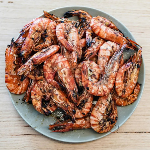 Grilled prawns, charred and seasoned with Gustus Vitaes Ultimate Gourmet BBQ Collection - 6 Tins, arranged on a gray plate atop a light wooden table.
