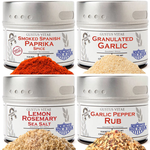 The Gustus Vitae Pantry Essentials Set includes 4 tins—Smoked Spanish Paprika Spice, Granulated Garlic, Lemon Rosemary Sea Salt, and Garlic Pepper Rub—each displayed with a small pile of gourmet sea salts or spices in front.