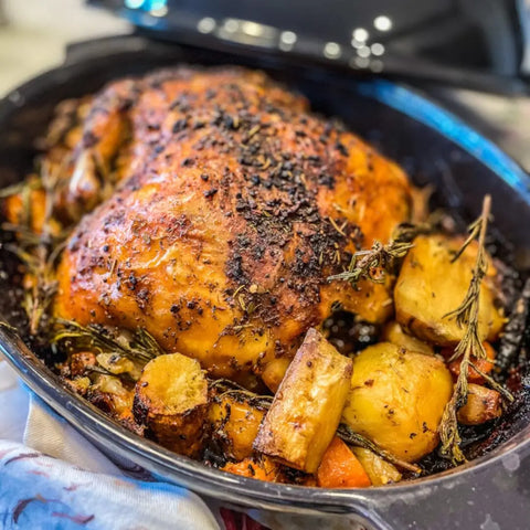 A golden-brown roasted chicken, seasoned with vendor-unknown Spring Party Essential Salts - 3 Pack, sits in a roasting pan surrounded by roasted potatoes, carrots, and fresh rosemary.