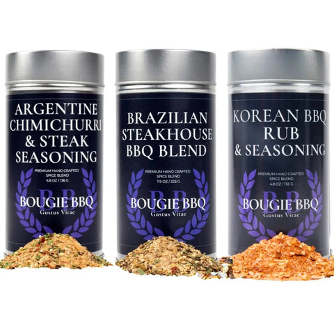 Three tins of Gustus Vitae Deluxe Steak & Beef BBQ Seasonings Collection—featuring Argentine Chimichurri & Steak, Brazilian Steakhouse BBQ Blend, and Korean BBQ Rub—with samples in front. Perfect for grilled steaks.