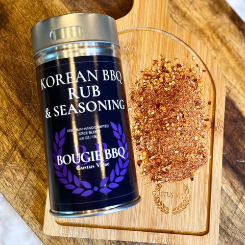 A tin from Gustus Vitaes Deluxe Steak & Beef BBQ Seasonings Collection - 3 Pack sits on a wooden cutting board beside a reddish spice blend—ideal for grilled steaks or as part of this artisanal seasoning set, on a dark wood surface.