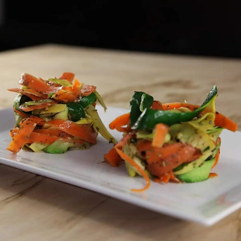Two small stacks of spiralized carrots and zucchini, seasoned with Gustus Vitae Luxury Protein & Fancy Truffled Side Seasonings (Set of 4), are arranged on a white rectangular plate atop a wooden surface.