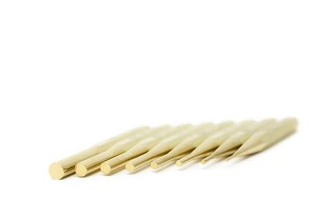 Seven gold-toned rods from the Grace USA Brass Pin Punch Set by Grace USA are arranged diagonally on a plain white surface, each piece decreasing in size from left to right for a minimalist display.