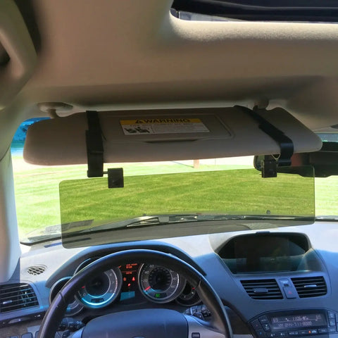 The Glare Guard Gray Polarized Car Visor Extender attaches to your visor above the dashboard, reducing sun glare for safer driving. Enjoy a clear view of green grass and trees outside.