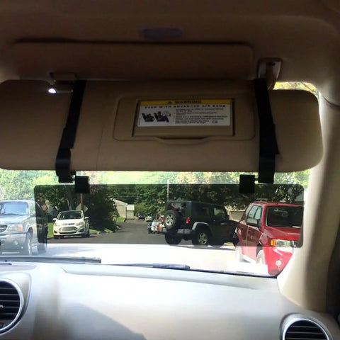 View from inside a parked car with the Glare Guard Gray Polarized Car Visor Extender and a tan visor with warning label down, providing glare-free driving as vehicles line a suburban street with trees and houses outside.