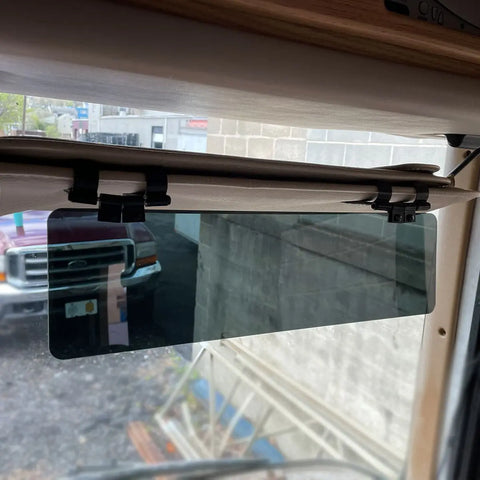 A Glare Guard Gray Polarized Truck Sun Visor Extender is installed above the windshield, with a truck and a concrete building visible outside through the glass.