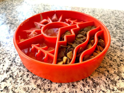 A red, segmented SodaPup Great Outdoors Design EBowl Enrichment Slow Feeder Bowl for Dogs with sections for kibble and water rests on a speckled countertop. Its raised patterns slow eating to support dog enrichment.