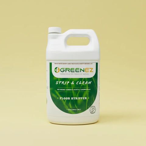 A white plastic 1-gallon jug of GreenEZ® Floor Stripper sits on a light yellow background. Its green and yellow label promotes this USA-made, eco-safe adhesive remover as free of harsh or caustic chemicals.