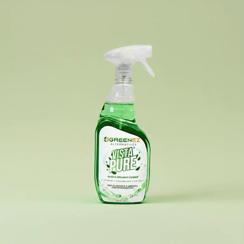 A clear spray bottle with green liquid, labeled GreenEZ® Vista Pure 22 Oz Glass Cleaner – Streak Free, stands against a light green background, showcasing an eco-friendly, USA-made cleaning solution for glass.